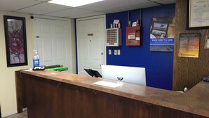 Un mostrador de recepción con una computadora, dispensador de gel antibacterial y un letrero que indica 'No Fumar'.