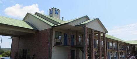 A two-story motel with a green roof, brick facade, and a covered parking area.