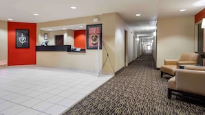 A hotel reception area with a reception desk, a framed picture, a red wall, and a carpeted hallway.