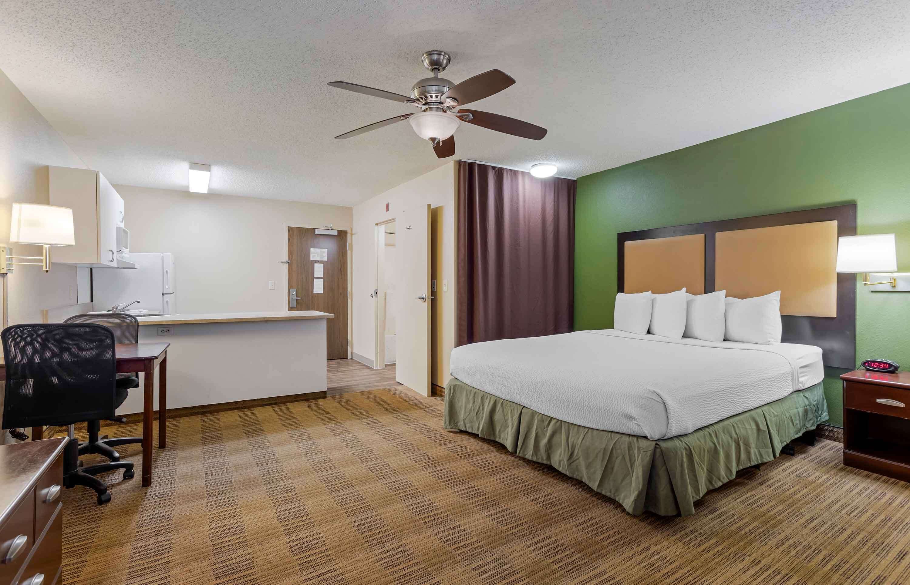 A hotel room with a bed, desk, chair, and a ceiling fan.