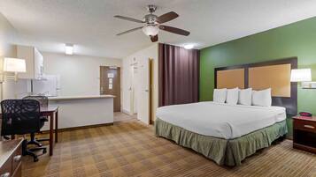 A hotel room with a bed, desk, chair, and a ceiling fan.