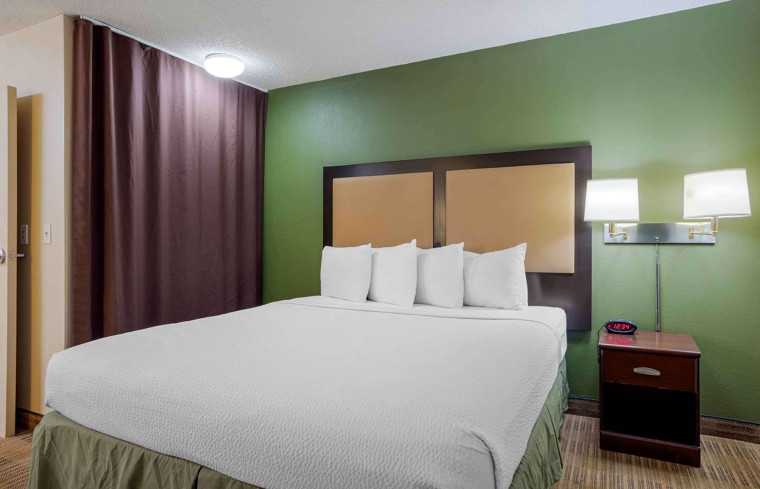 A hotel room with a large bed, a nightstand with a clock, and a green wall.