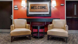 A lobby with two leather armchairs, a small round table, a welcome sign, and a red wall.