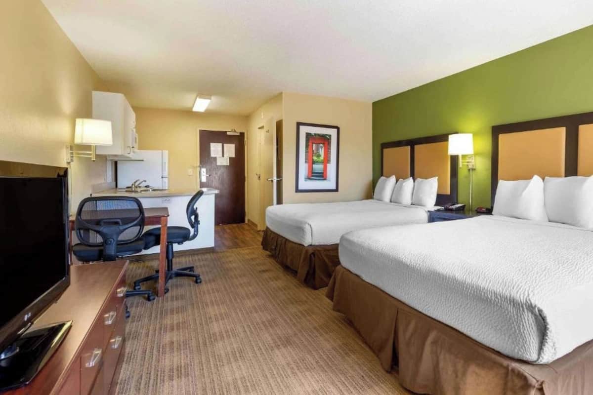 A hotel room with two beds, a desk with a chair, a television, and a framed picture on the wall.