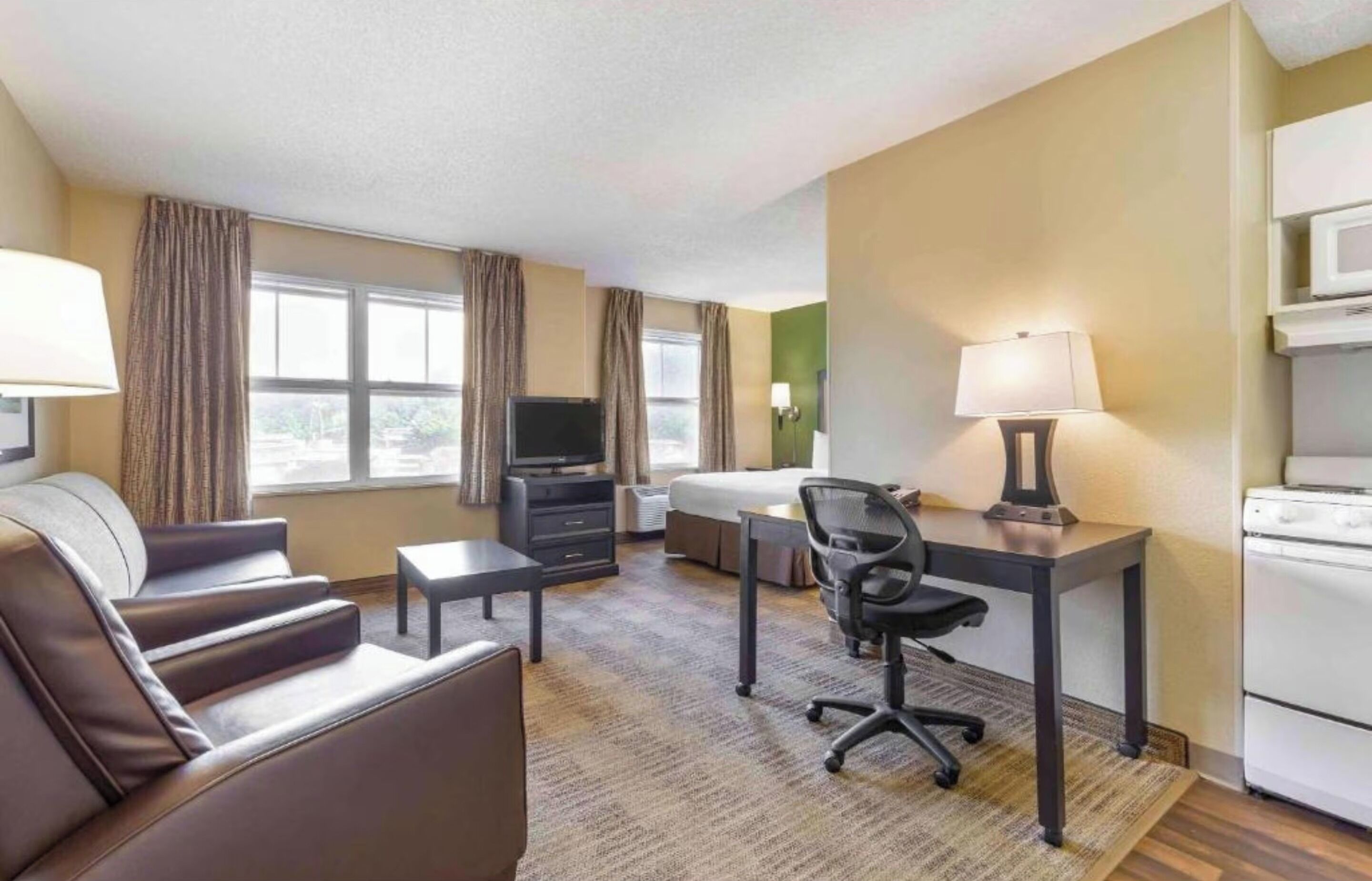 Ein Hotelzimmer mit Sofa, Schreibtisch, Stuhl, Fernseher, Bett, Lampe und einer Mikrowelle.