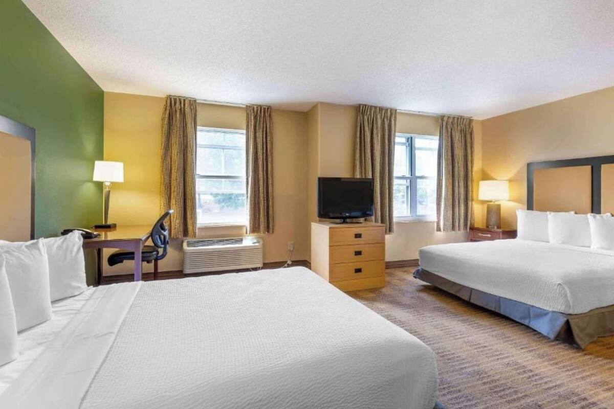 A hotel room with two beds, a desk with a chair, a TV, and a dresser.