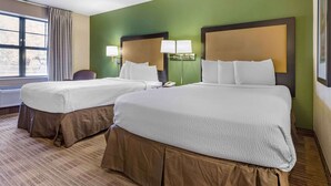 Habitación de hotel con dos camas, una ventana con cortinas, una silla y un escritorio con lámpara.