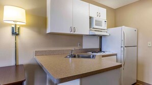 Una cocina compacta con armarios blancos, un lavamanos de acero inoxidable, un microondas y un refrigerador.
