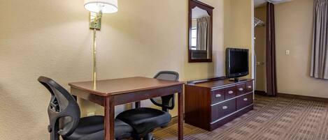A hotel room with a desk, two chairs, a lamp, a television, a mirror, and a wardrobe.