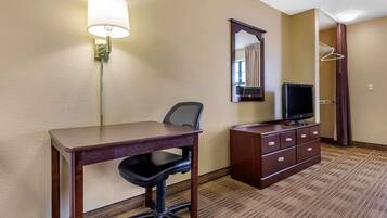 Una habitación de hotel con escritorio, silla, televisor, cómoda, espejo y perchero.
