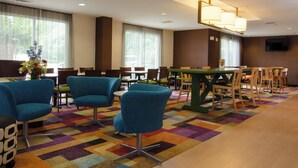 A hotel lobby with teal chairs, a green table, and a colorful carpet.