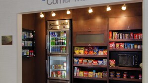 A kitchenette area with a refrigerator, microwave, and shelves stocked with snacks and beverages.