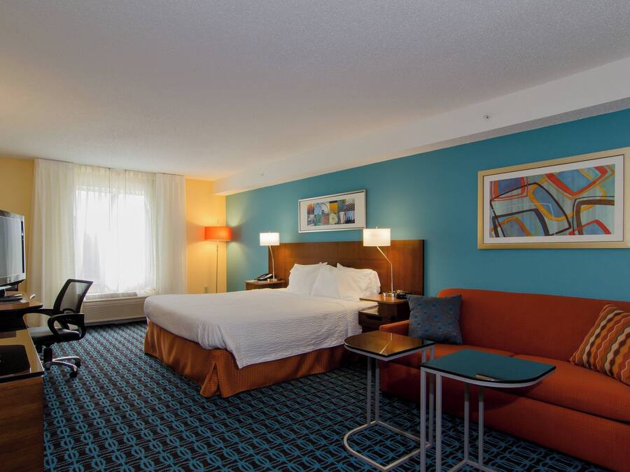A hotel room with a bed, a desk with a computer, a TV, a sofa, and two side tables.