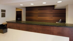 A hotel reception desk with a wooden panel wall, a black countertop, and a trash bin.