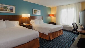 A hotel room with two beds, a desk with a television, a chair, and a window with curtains.