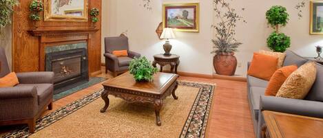 A cozy living room with a fireplace, comfortable seating, and decorative plants.