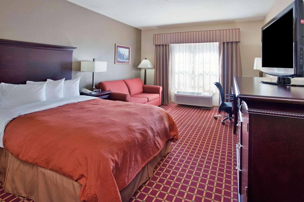A hotel room with a large bed, a desk, a chair, a television, and a window with curtains.