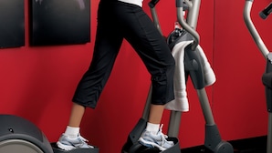 A woman using a stationary bike in a gym with red walls and multiple exercise machines. - Country Inn & Suites by Radisson, Columbia, SC (Columbia)