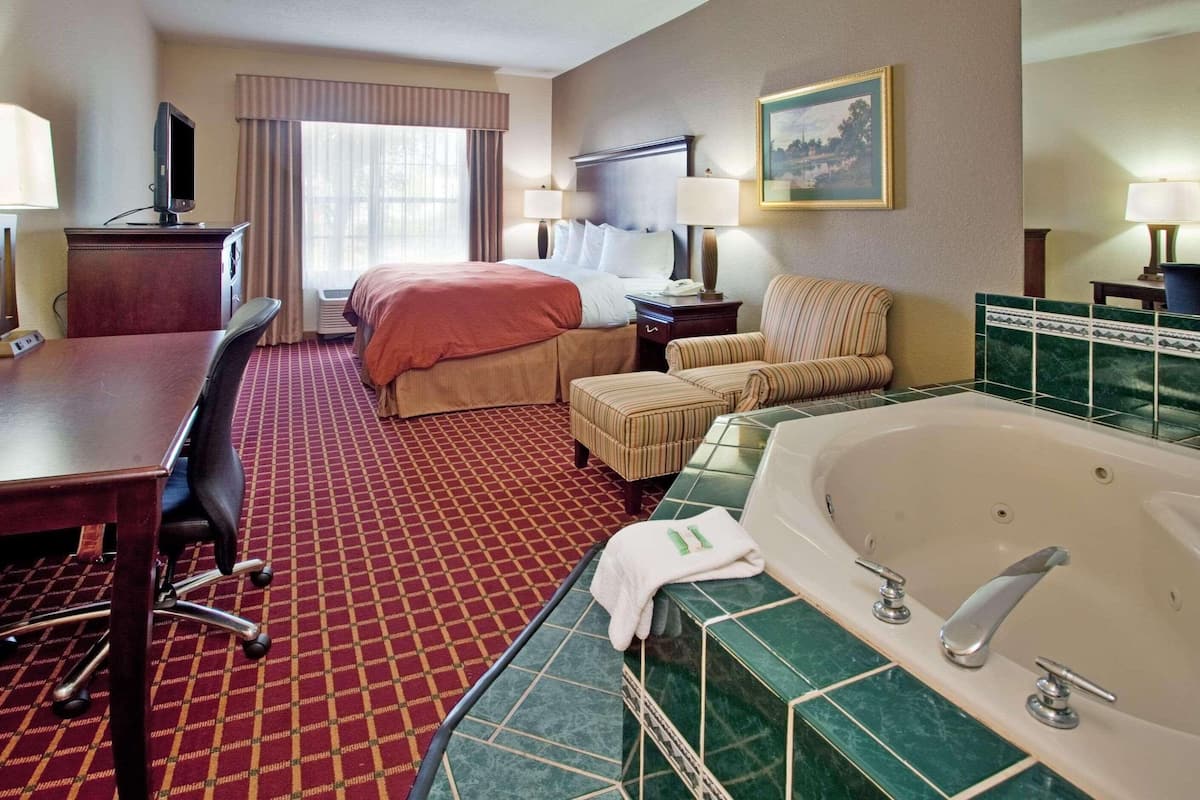 A hotel room with a bed, a desk, a chair, a sofa, a bathtub, and a television.