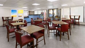 A dining area with multiple tables and chairs, a vending machine, and a view of the outside through large windows. - Days Inn by Wyndham Tonawanda/Buffalo (Tonawanda)
