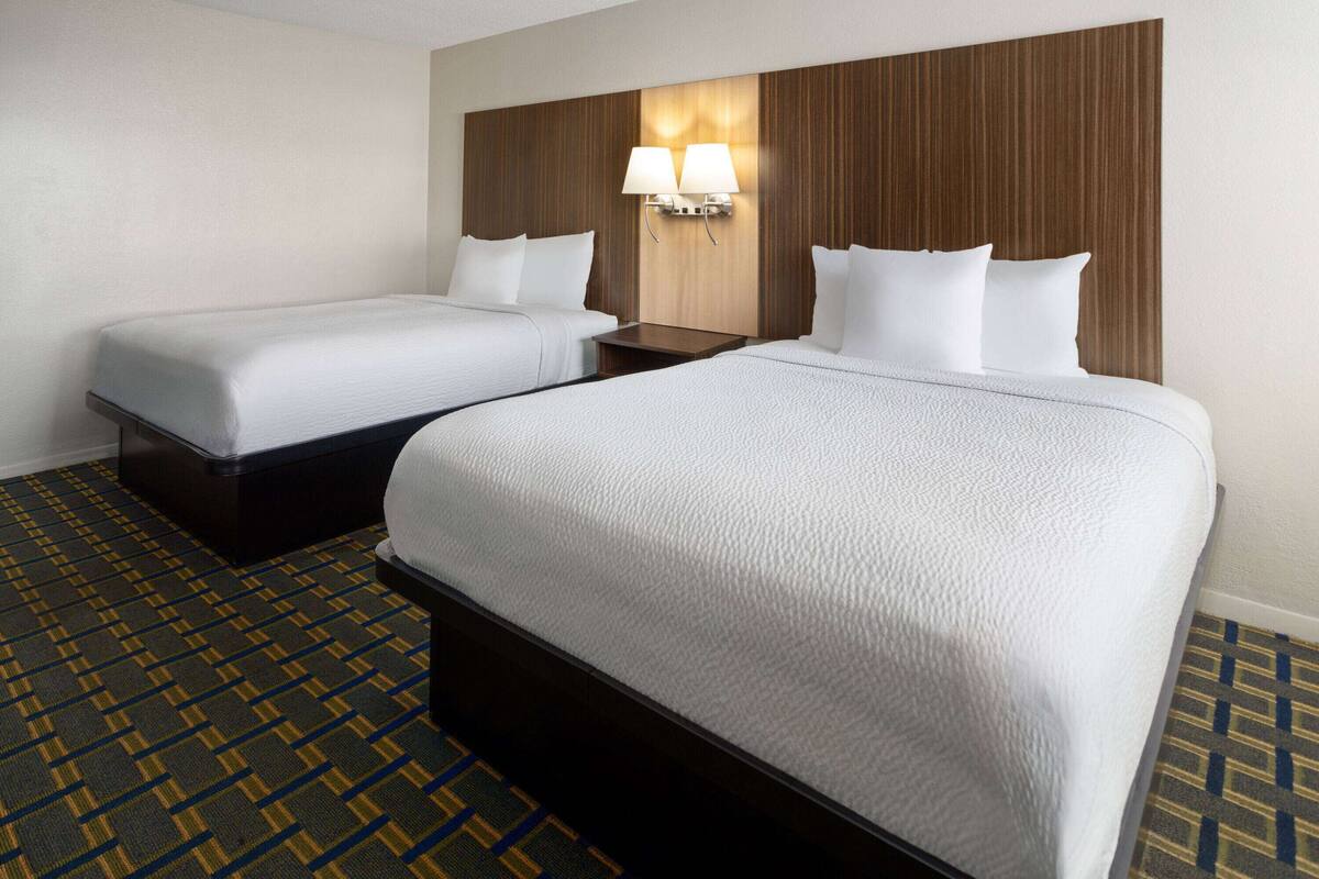 Une chambre d’hôtel avec deux lits simples, une tête de lit en bois, deux lampes de chevet et une moquette à motifs.