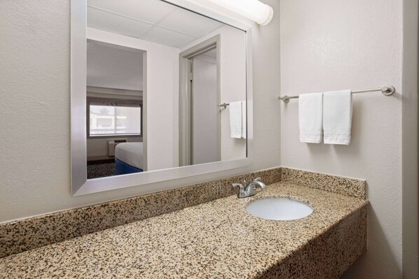 Une salle de bain avec un comptoir en granit, un lavabo, un miroir et un porte-serviettes avec deux serviettes.