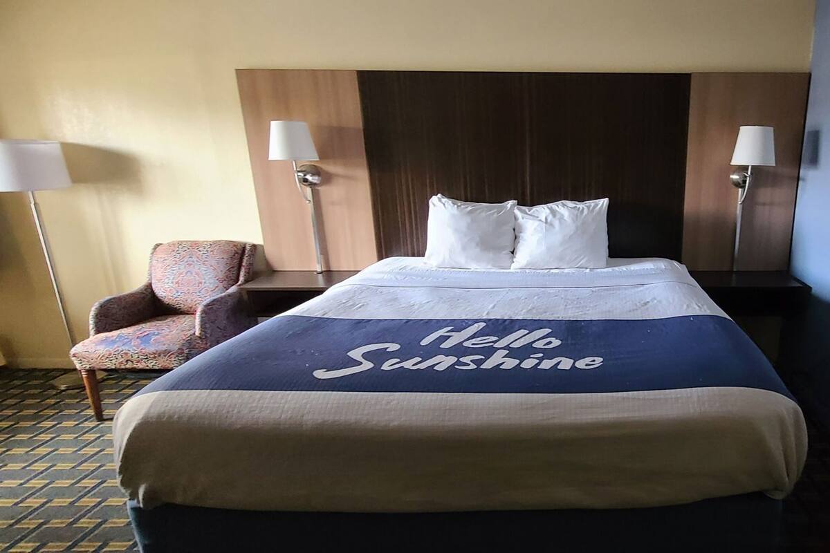 Une chambre d’hôtel avec un lit, deux lampes de chevet, une chaise et un mur avec une porte.