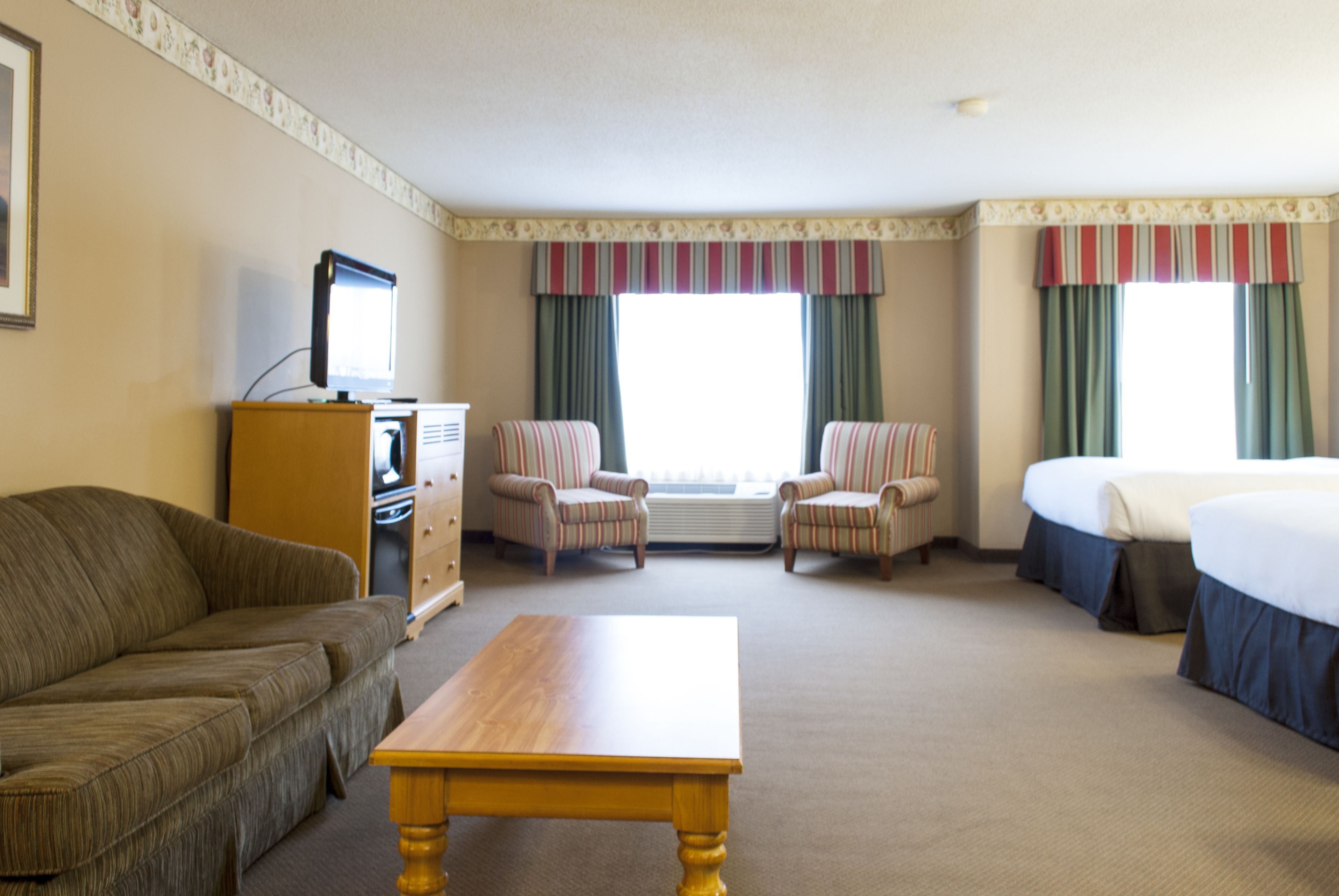 Une chambre d’hôtel comprenant un canapé, deux fauteuils, une table en bois, un lit, une télévision et une commode.