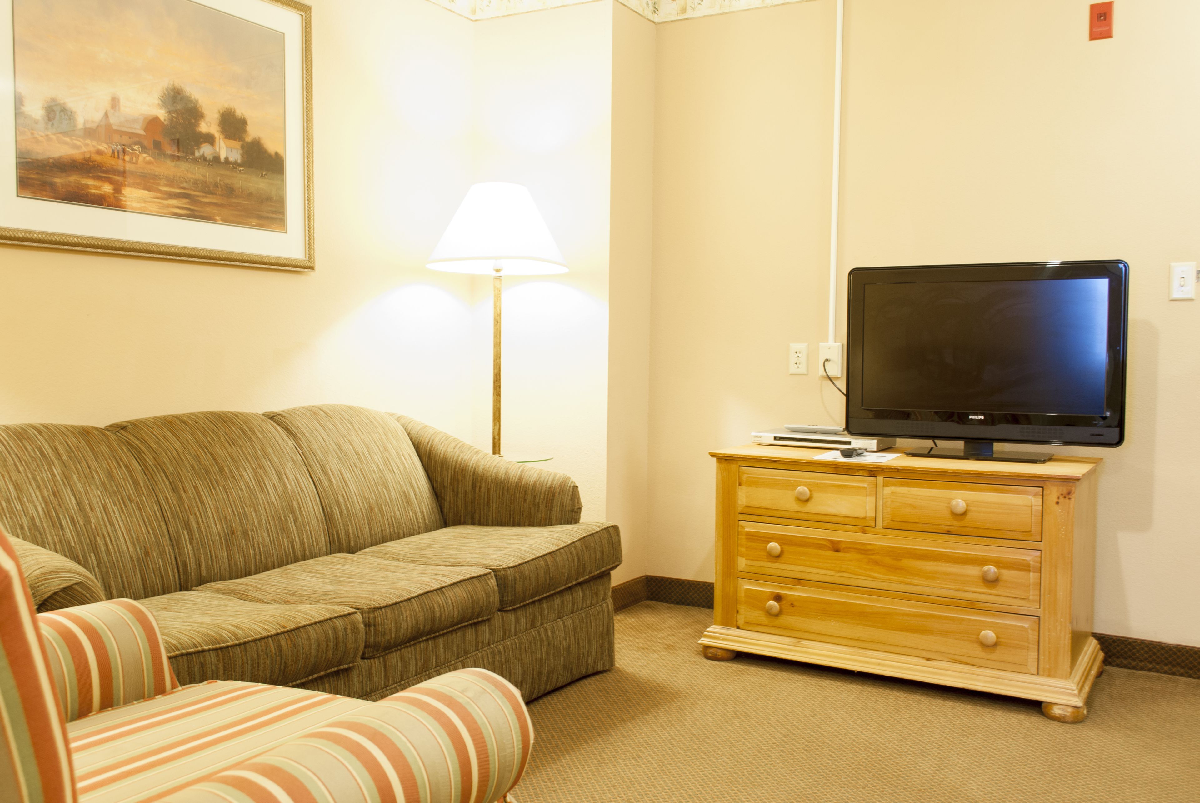 A living room with a sofa, a television on a wooden dresser, and a lamp.