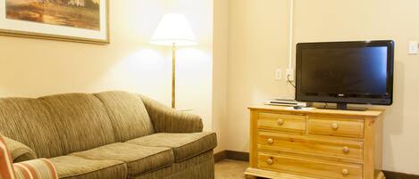 A living room with a sofa, a television on a wooden dresser, and a lamp.