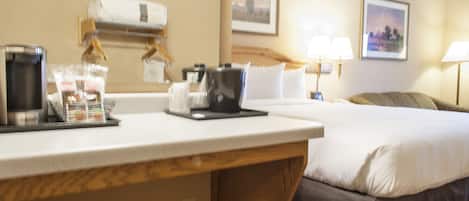 A hotel room with a bed, a desk with a coffee maker, a lamp, and a picture on the wall.