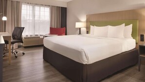 A hotel room with a large bed, a desk with a chair, a red chair, a lamp, and a window with curtains. - Country Inn & Suites by Radisson, Cedar Falls, IA (Cedar Falls)