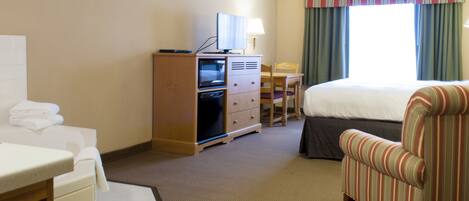 A hotel room with a bed, a desk with a computer, a chair, and a television on a cabinet.