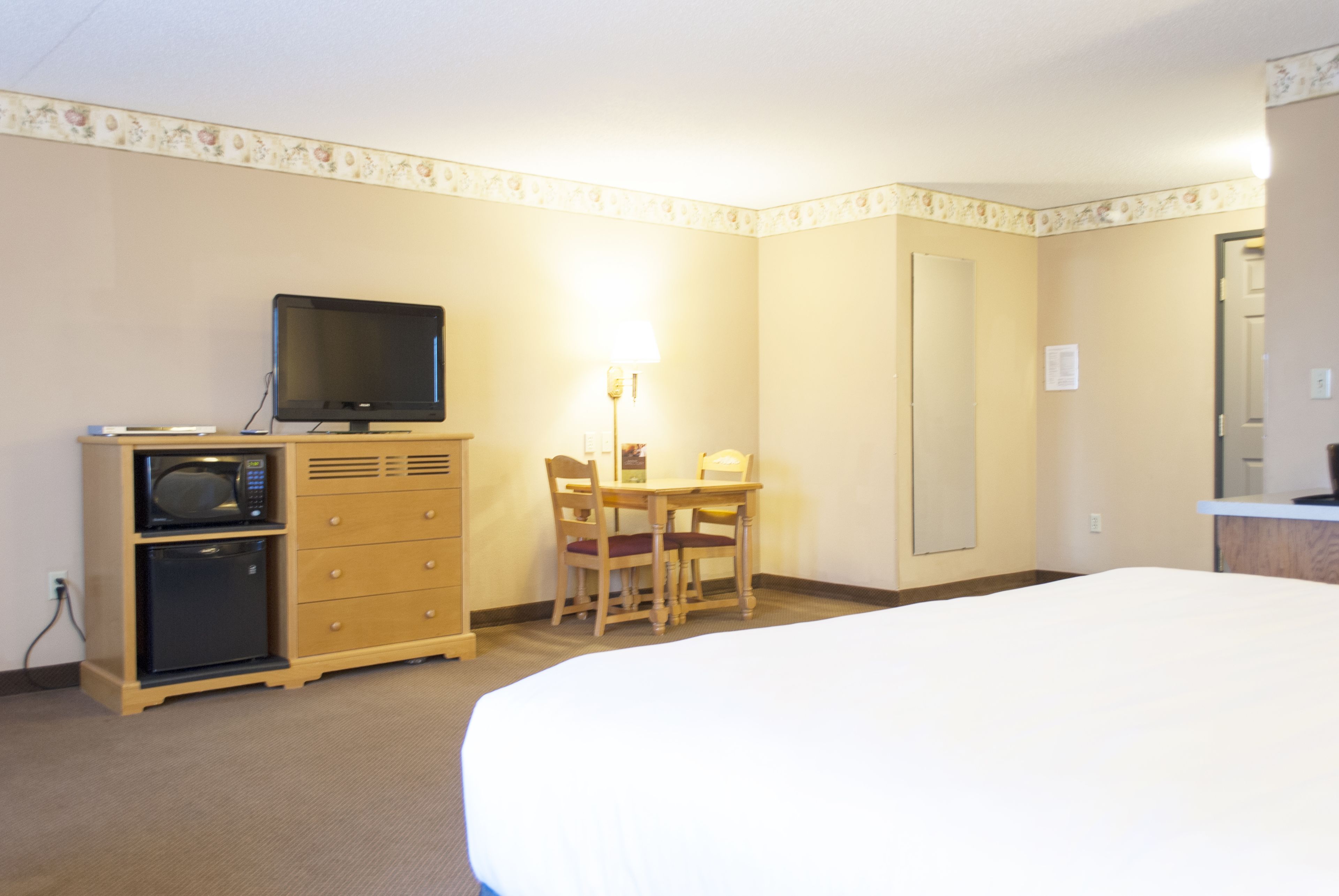 A hotel room with a bed, a desk with a chair, a television, and a microwave.
