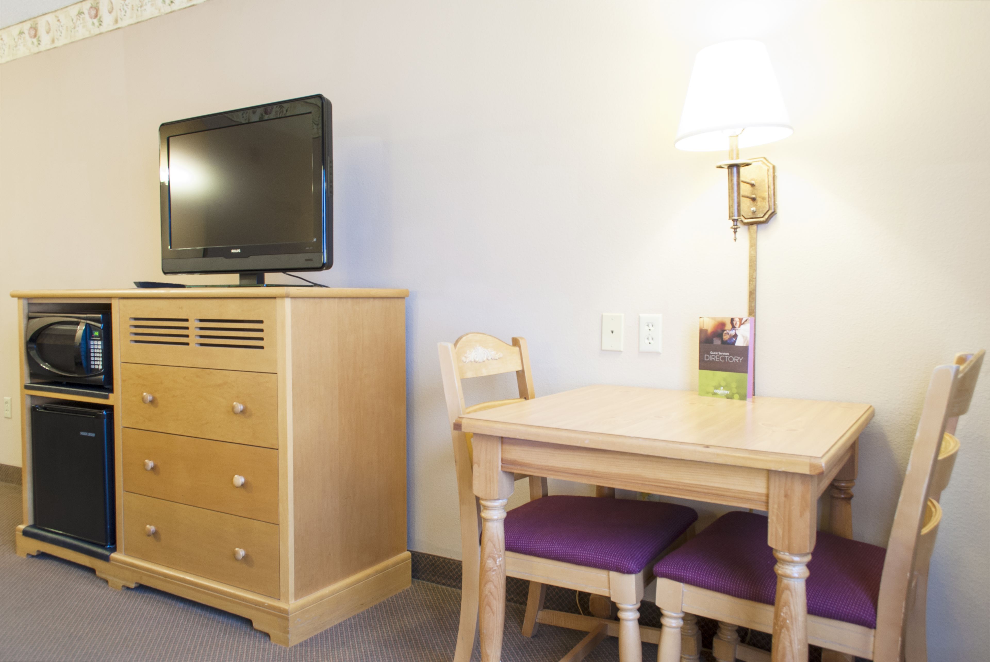 A hotel room with a wooden cabinet, a television, a table with two chairs, and a lamp.