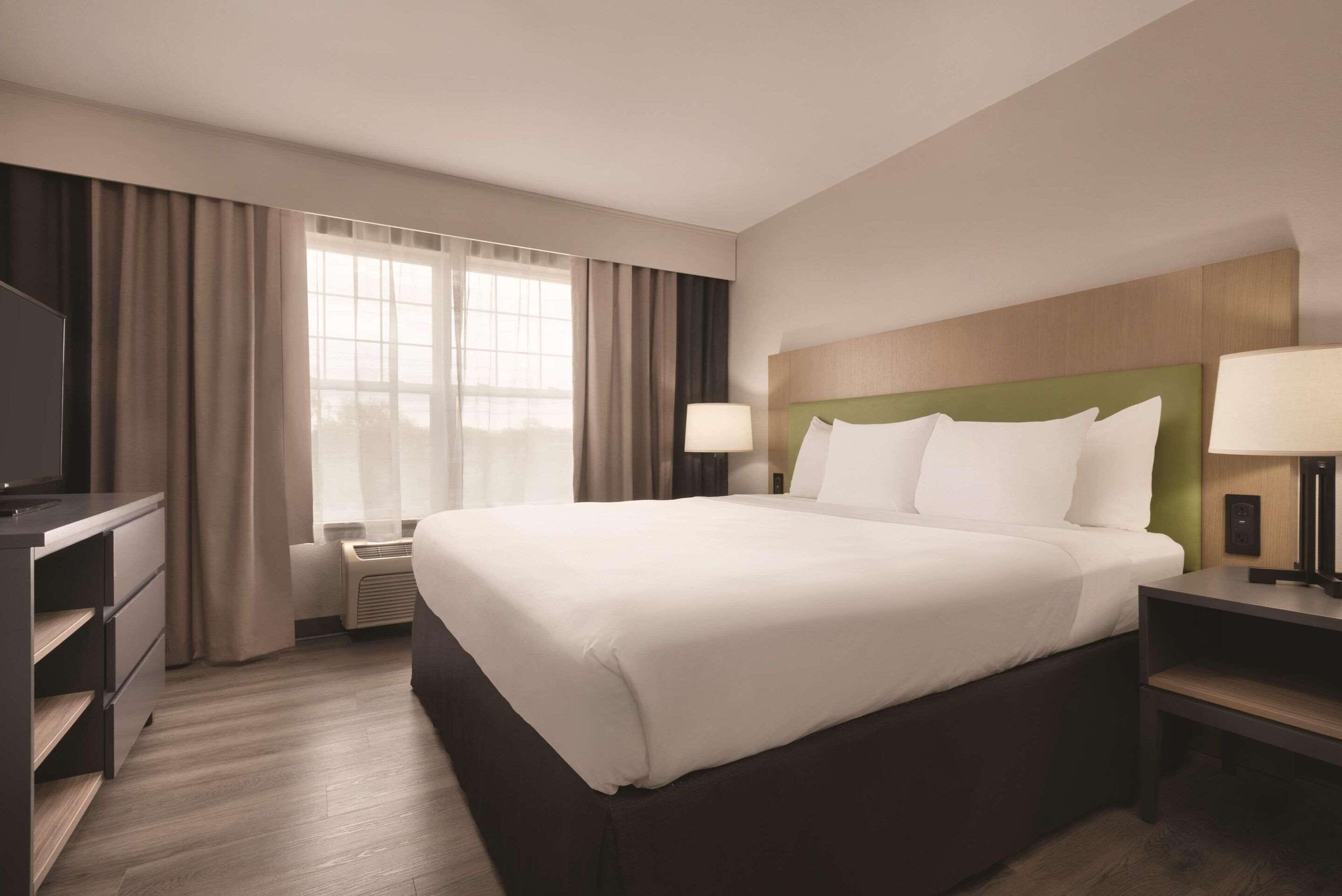 A hotel room with a large bed, a desk with a chair, a TV, and a window with curtains.