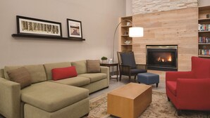 A living room with a sectional sofa, a red armchair, a coffee table, a fireplace, and a bookshelf. - Country Inn & Suites by Radisson, Cedar Falls, IA (Cedar Falls)
