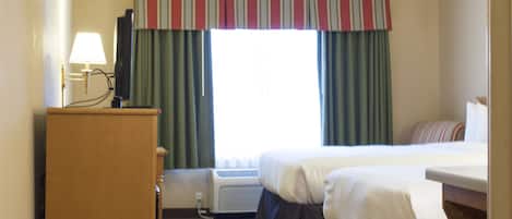 A hotel room with a bed, a desk with a lamp, and a window with curtains.
