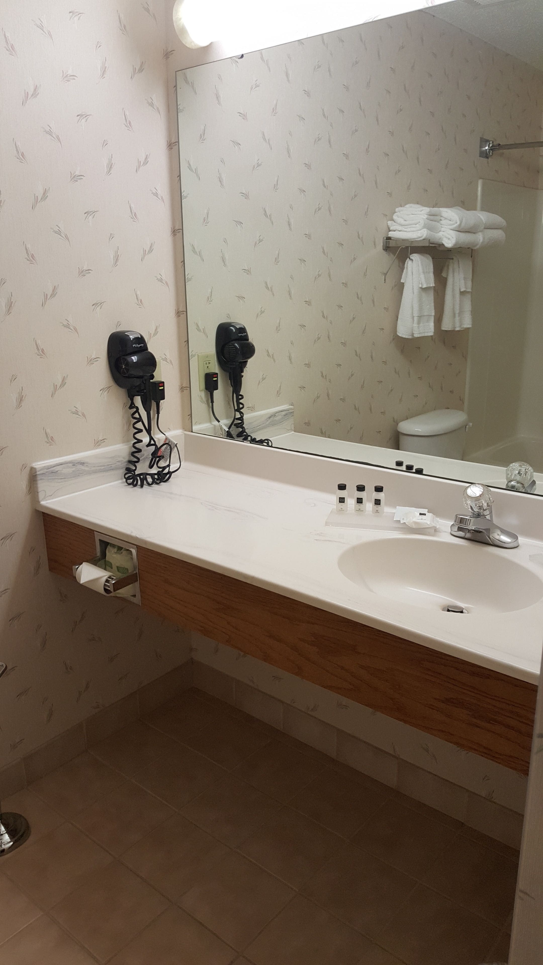 Un baño con lavamanos blanco, espejo y toallero.