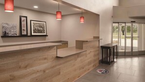 A reception area with a wooden reception desk, framed artwork on the wall, and a glass door leading outside. - Country Inn & Suites by Radisson, Cedar Falls, IA (Cedar Falls)