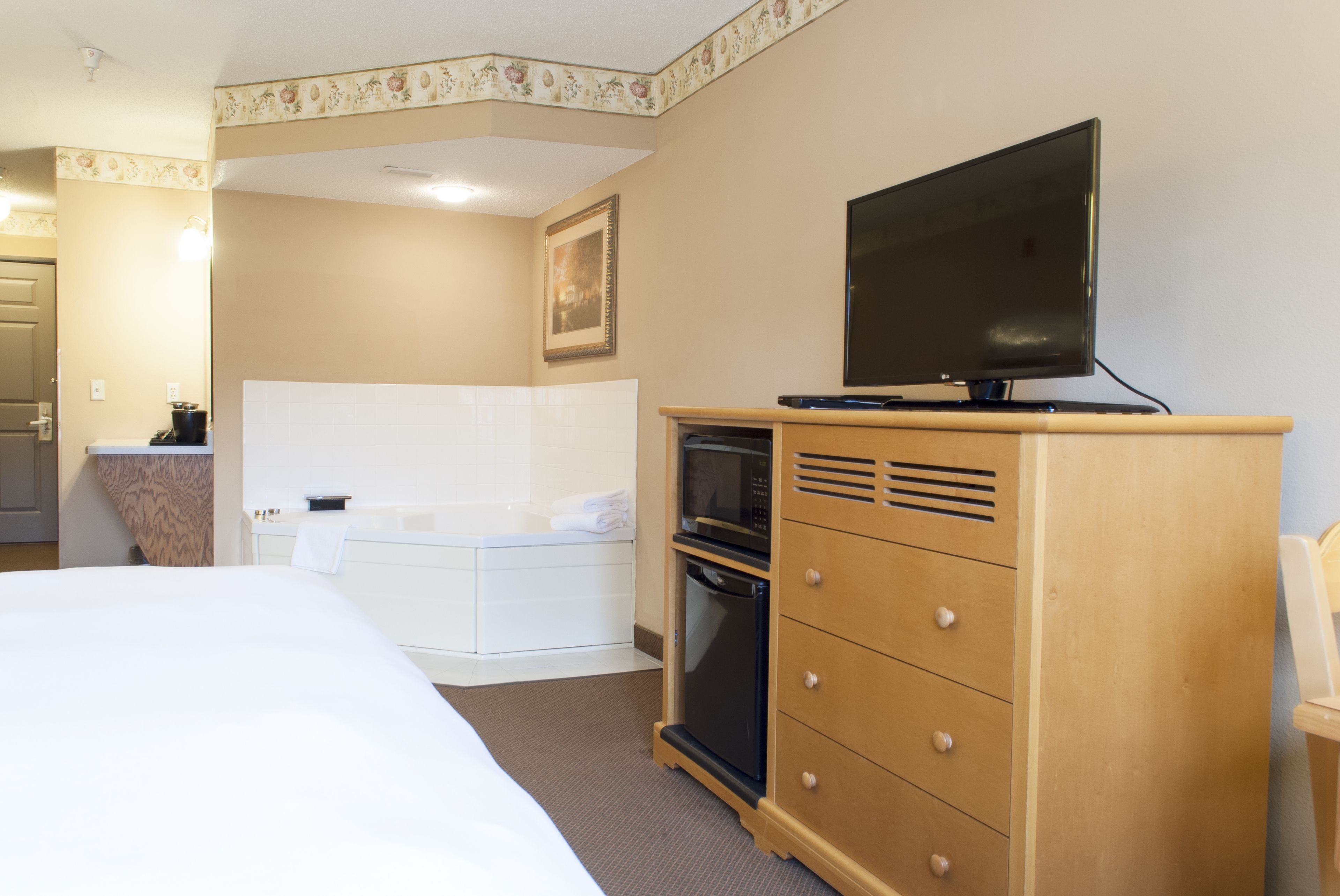 A hotel room with a bed, a wooden dresser with a flat-screen TV, a microwave, and a small oven.