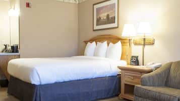 Habitación de hotel con una cama grande, una mesita de noche con lámpara, una silla y un cuadro en la pared.