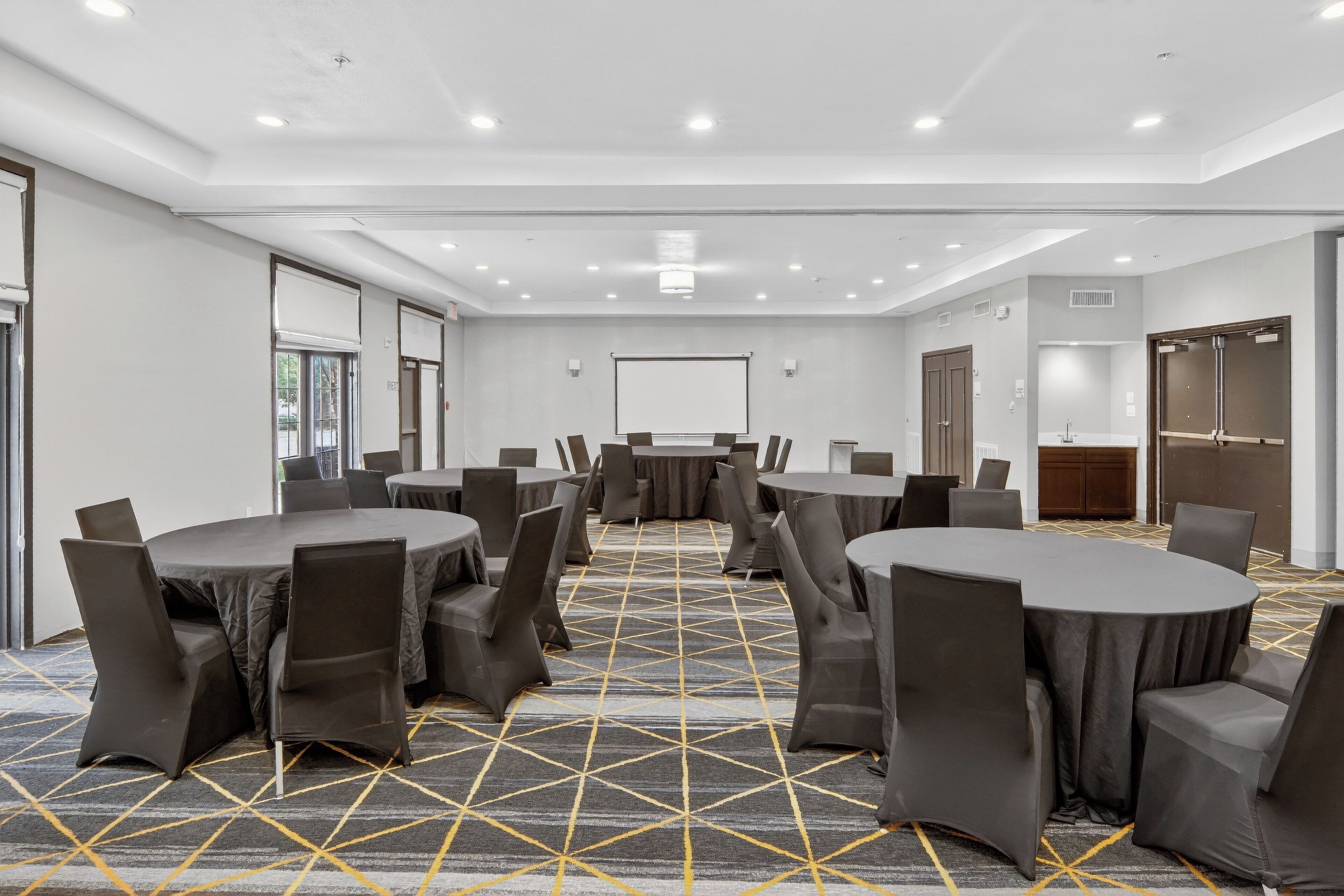 A conference room with round tables and chairs, a projector screen, and a carpeted floor.