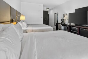 A hotel room with two beds, a desk with a computer, a TV, and a lamp.