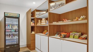 A refrigerated beverage dispenser, a welcome sign, and snack shelves in a hotel lobby. - Holiday Inn & Suites Dallas-Addison by IHG (Addison)