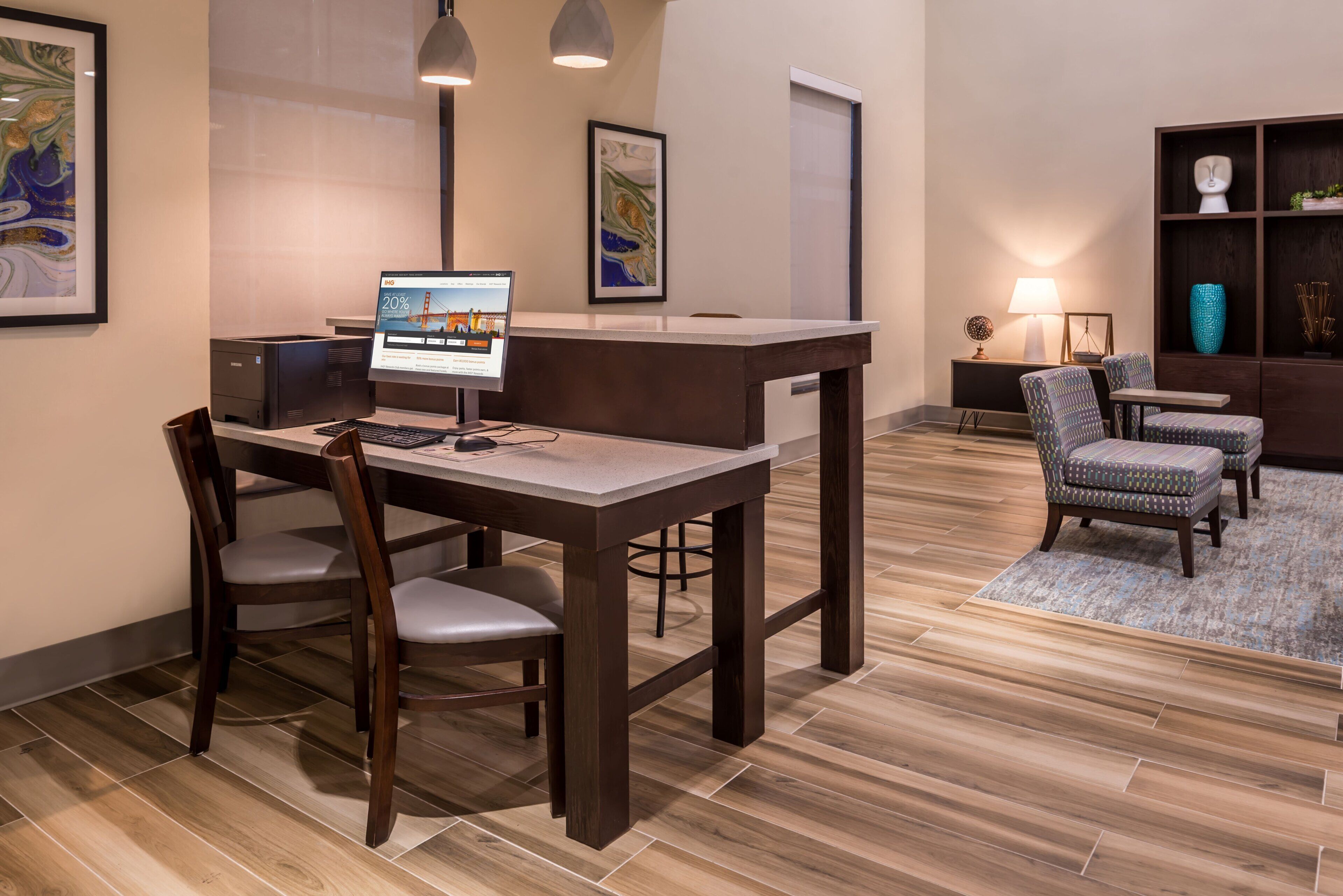 A hotel reception area with a desk, chairs, a computer, and framed artwork on the walls.