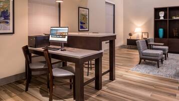 A hotel reception area with a desk, chairs, a computer, and framed artwork on the walls.