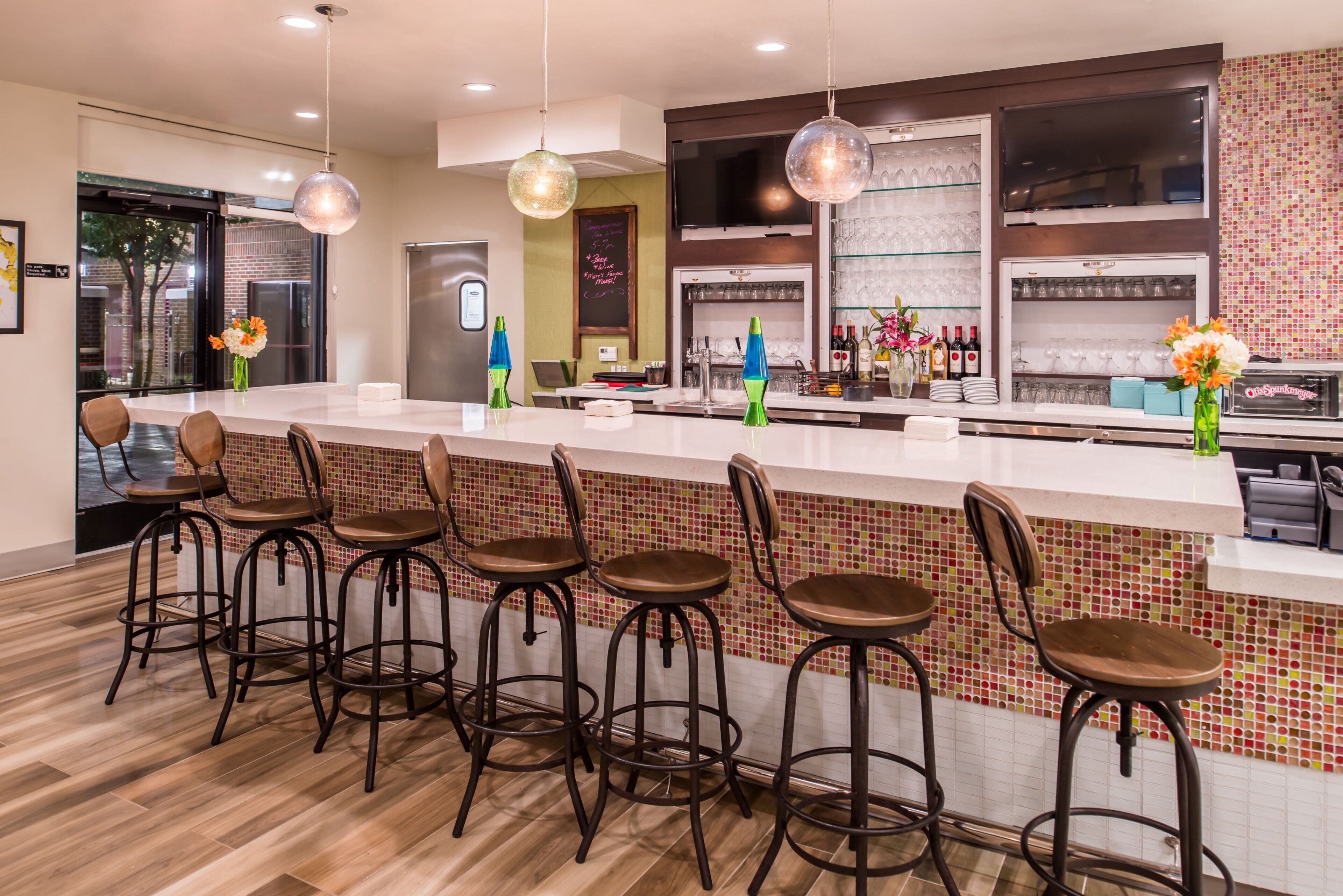 A modern bar area with a long counter, bar stools, and a variety of glassware and bottles.