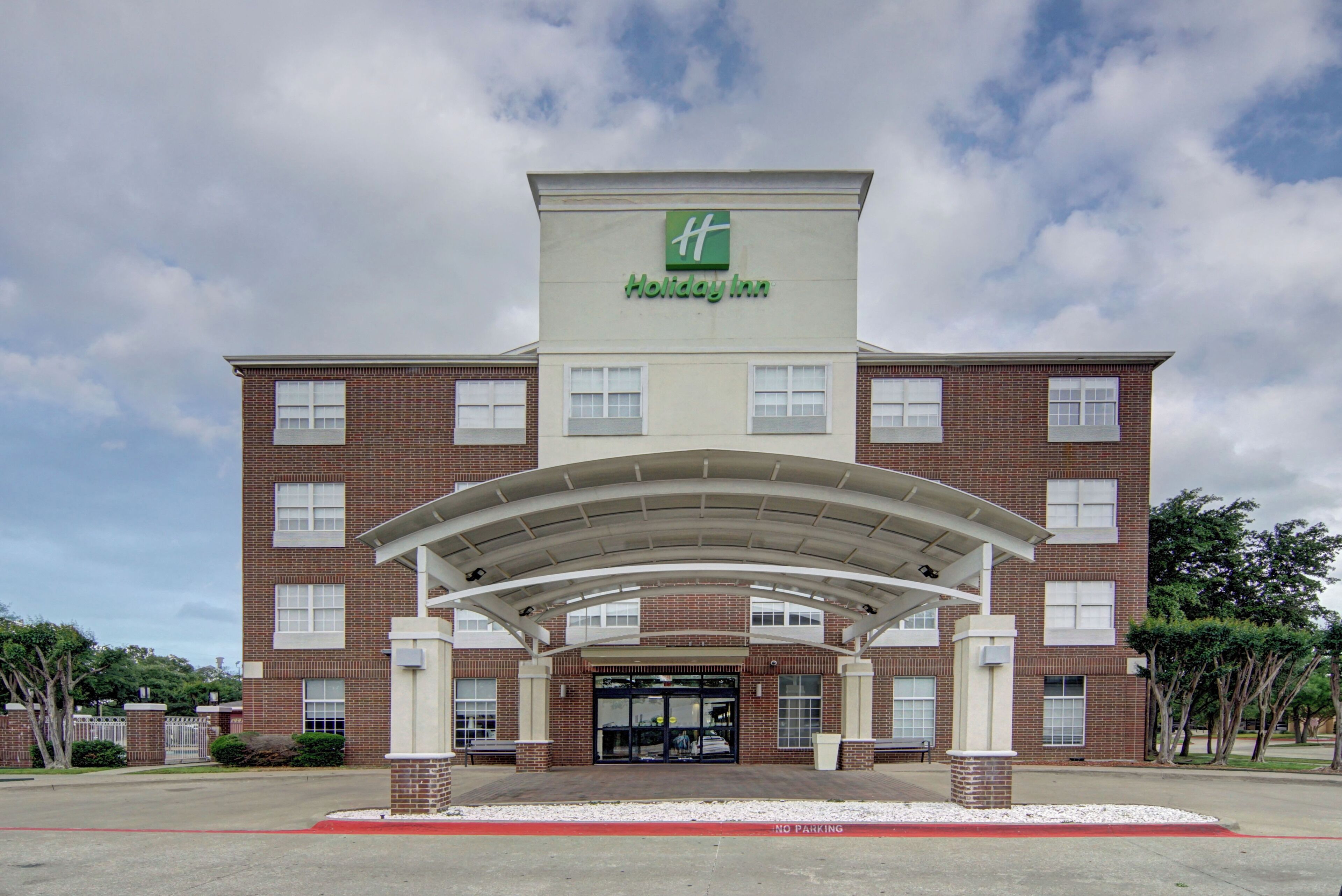 Un hotel Holiday Inn con fachada de ladrillo, un acceso cubierto y un cielo despejado.