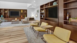 A modern living room with a flat-screen TV, wooden shelving, and comfortable seating. - Holiday Inn & Suites Dallas-Addison by IHG (Addison)